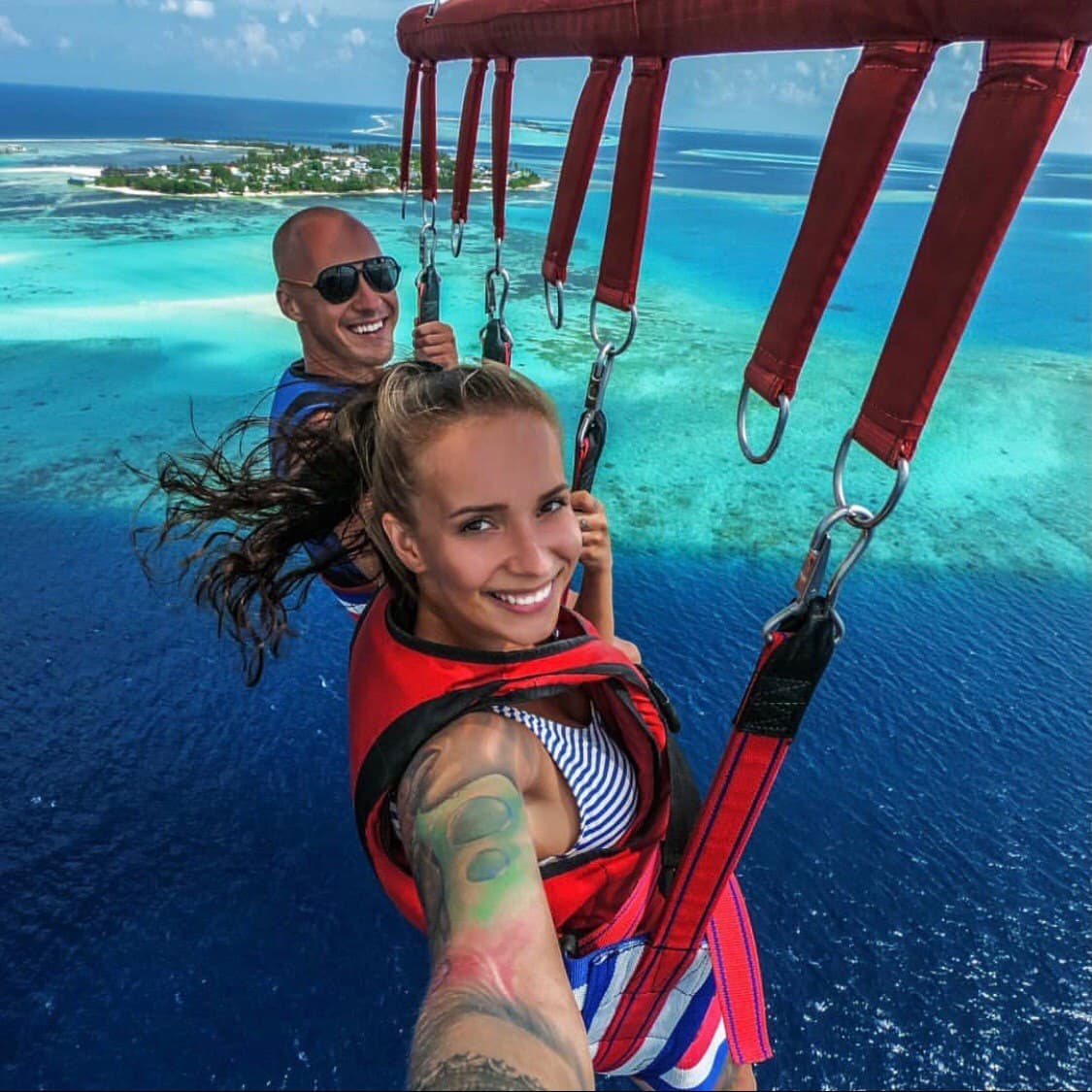 Smiling couple parasailing high above the turquoise Maldivian islands, showcasing unique experiences offered by Arriva Maldives Speedboat Transfer Company.